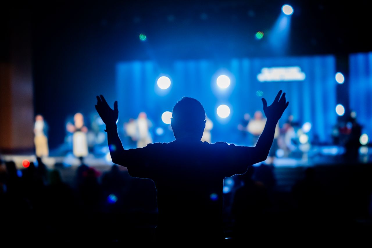 Silhouette of a person with raised hands at a vibrant concert stage.