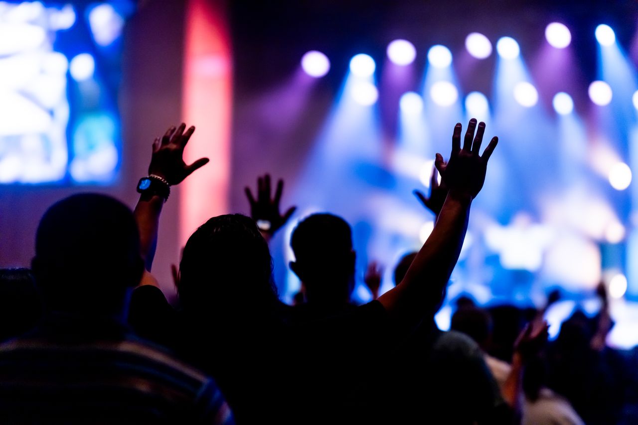 Engaged crowd enjoying a live concert with colorful stage lights and raised hands.